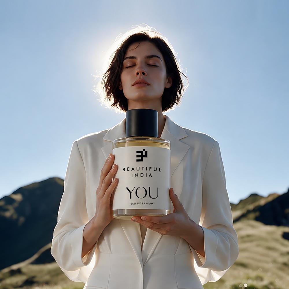 A woman holding You Eau de Parfum before sunlit mountains